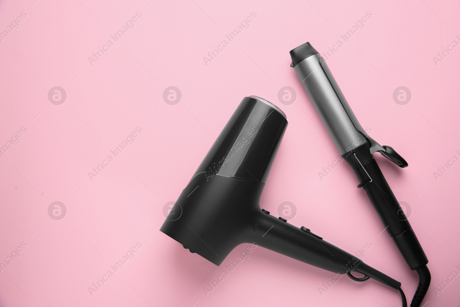 Photo of Hair dryer and curling iron on pink background, top view. Space for text