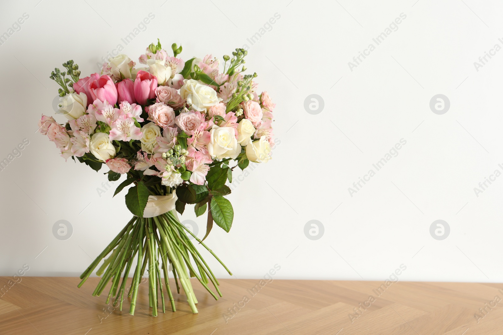 Photo of Beautiful bouquet of fresh flowers on wooden table near white wall, space for text