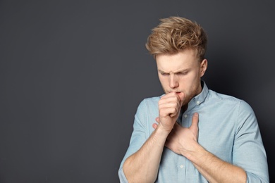 Handsome young man coughing against dark background. Space for text