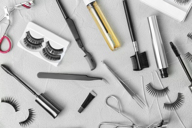 Flat lay composition with false eyelashes, cosmetic products and tools on grey background