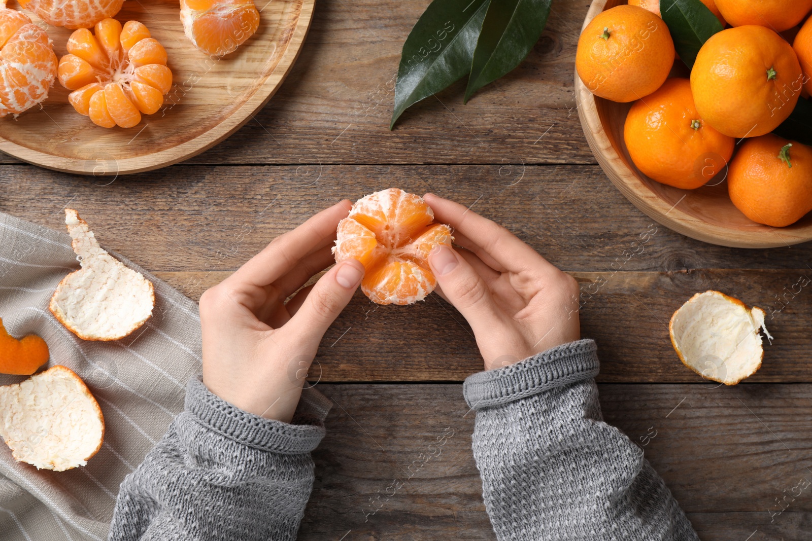 Photo of Woman holding peeled ripe tangerine at wooden table, top view