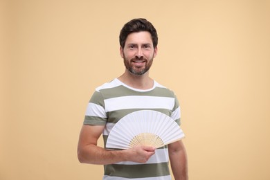 Happy man holding hand fan on beige background