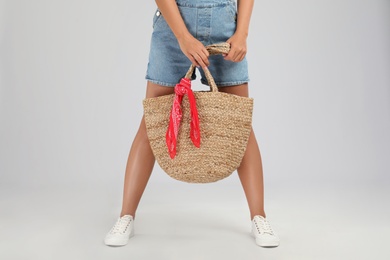 Young woman with stylish straw bag on light grey background, closeup