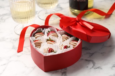 Photo of Delicious chocolate covered strawberries in heart shaped box and sparkling wine on white marble table