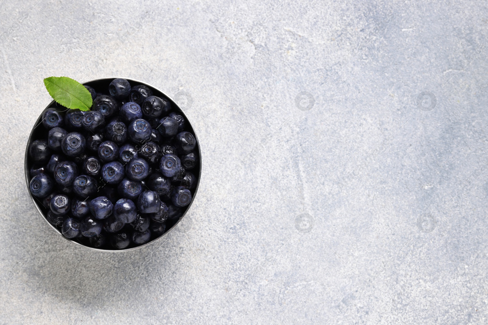 Photo of Ripe bilberries and leaf in bowl on light grey textured table, top view. Space for text