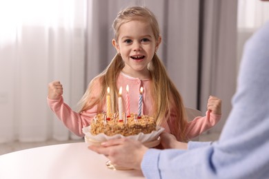 Birthday celebration. Mother holding tasty cake with burning candles near her daughter indoors