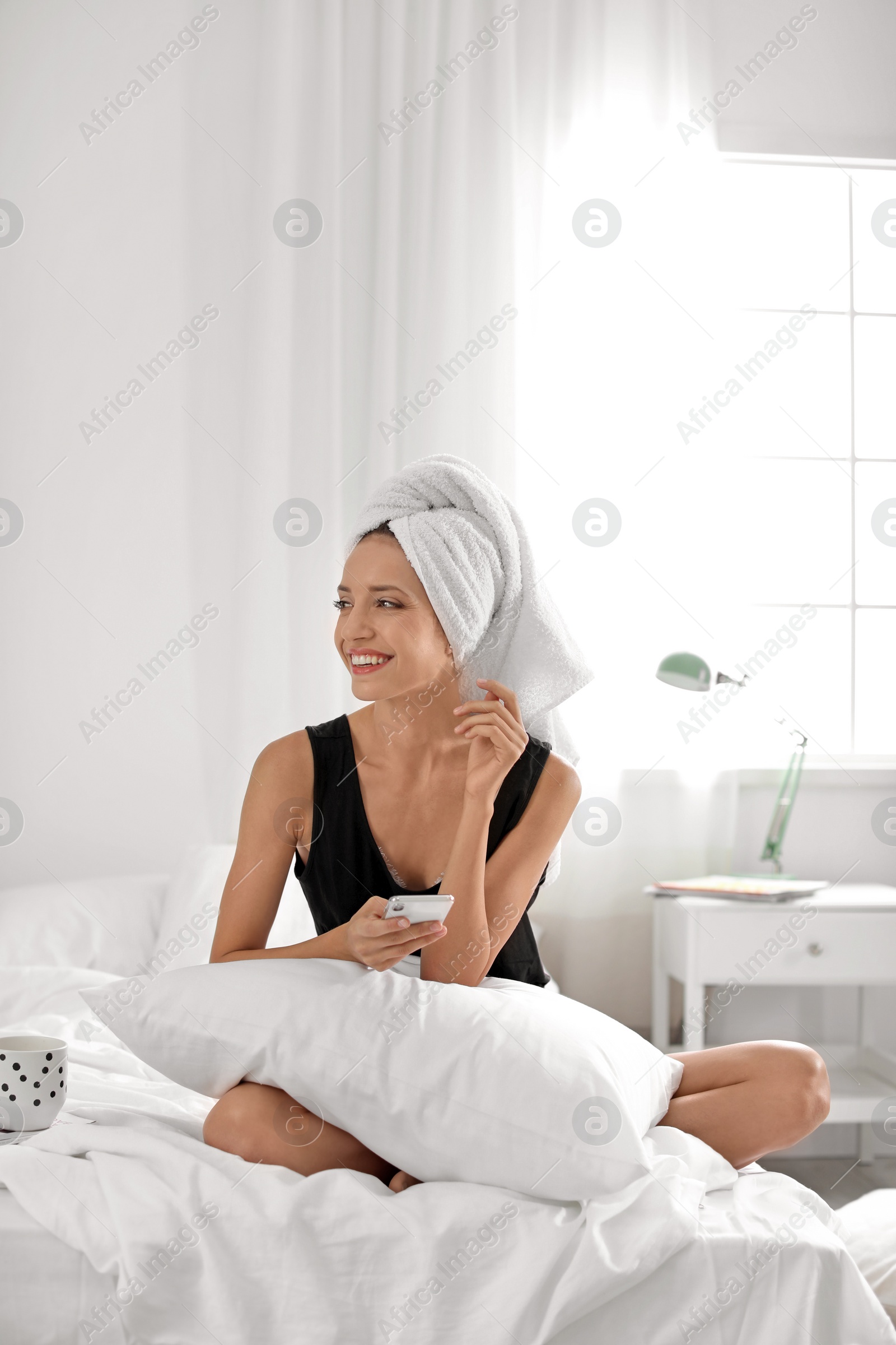 Photo of Young happy woman with mobile phone on bed at home. Lazy morning