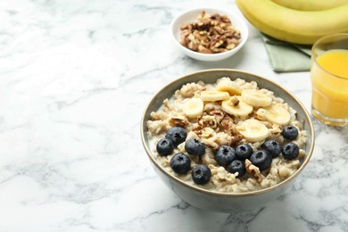 Tasty oatmeal with banana, blueberries, walnuts and milk served in bowl on white marble table, space for text