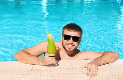 Photo of Young bearded man with refreshing cocktail in swimming pool at resort