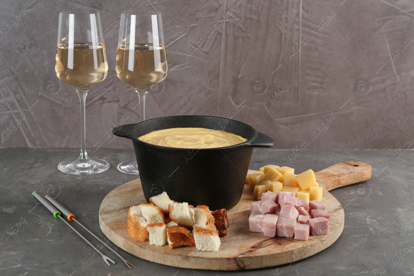 Photo of Fondue pot with tasty melted cheese, forks, wine and different snacks on grey table