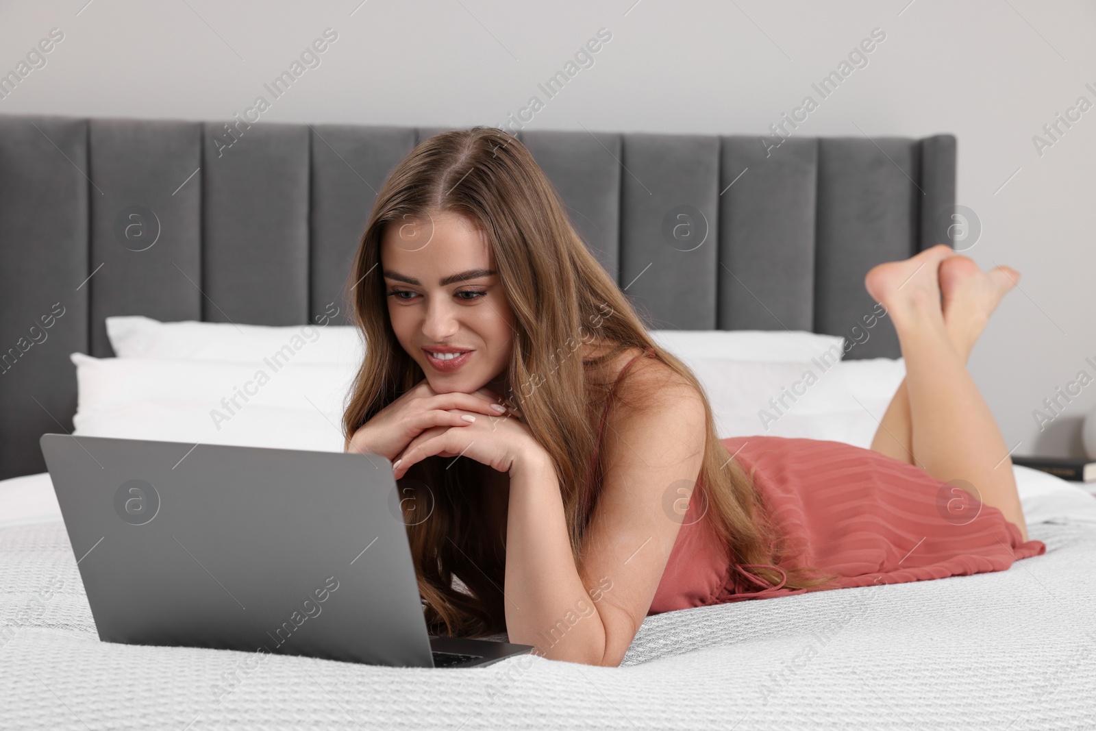 Photo of Happy woman with laptop on bed in bedroom