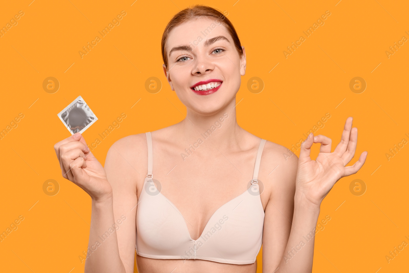 Photo of Woman in bra with condom showing ok gesture on yellow background. Safe sex