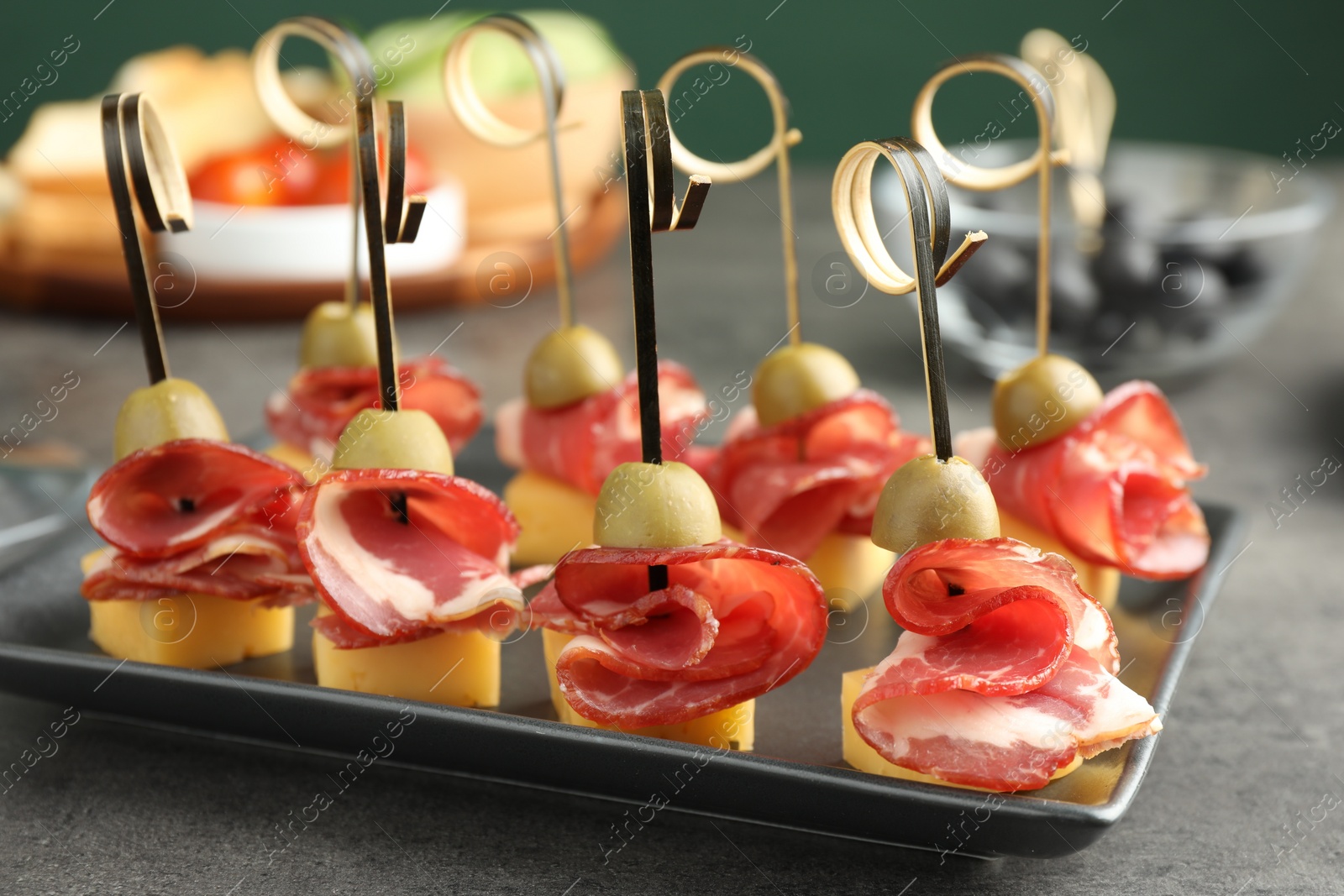 Photo of Tasty canapes with olives, prosciutto and cheese on grey table, closeup