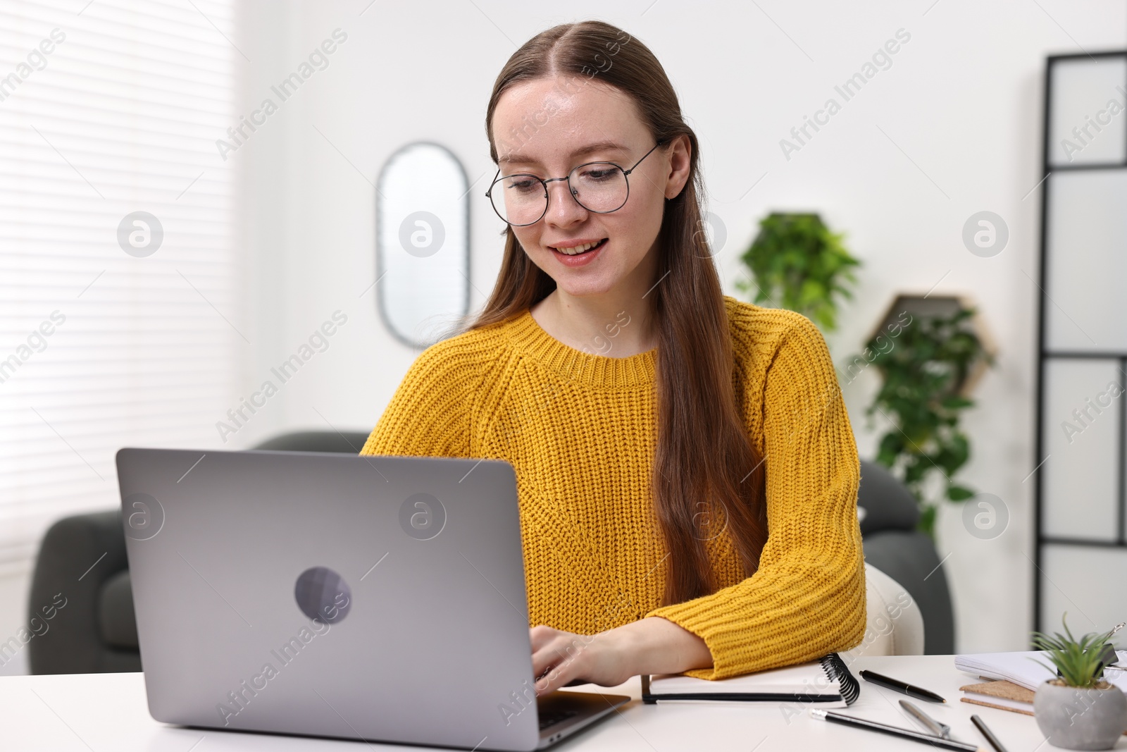 Photo of E-learning. Young woman using laptop during online lesson at white table indoors