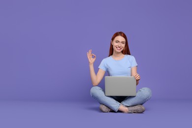 Photo of Smiling young woman with laptop showing OK gesture on lilac background, space for text