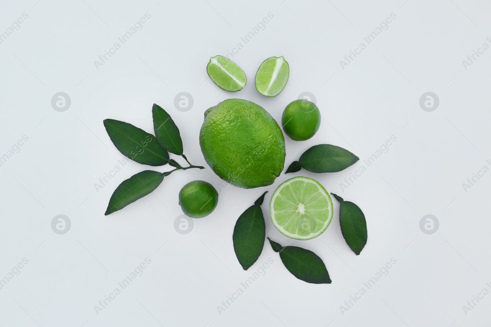 Photo of Whole and cut fresh limes with leaves on white background, flat lay