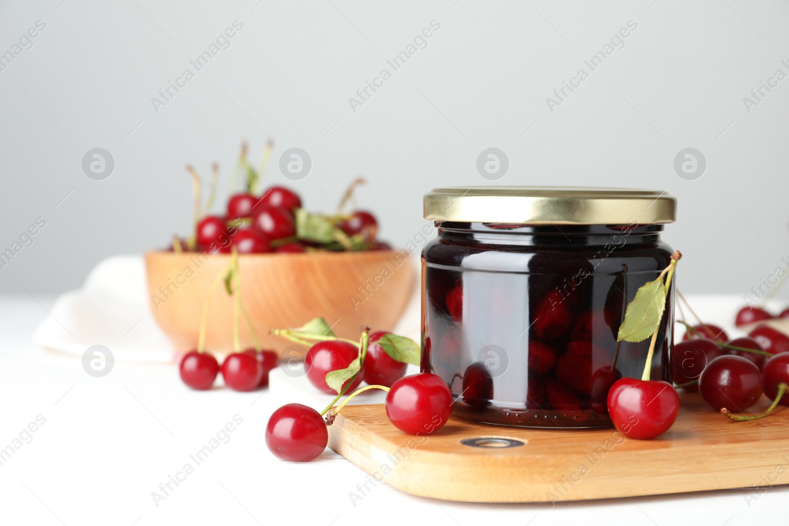 Photo of Jar of pickled cherries and fresh fruits on white table