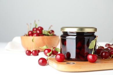 Jar of pickled cherries and fresh fruits on white table