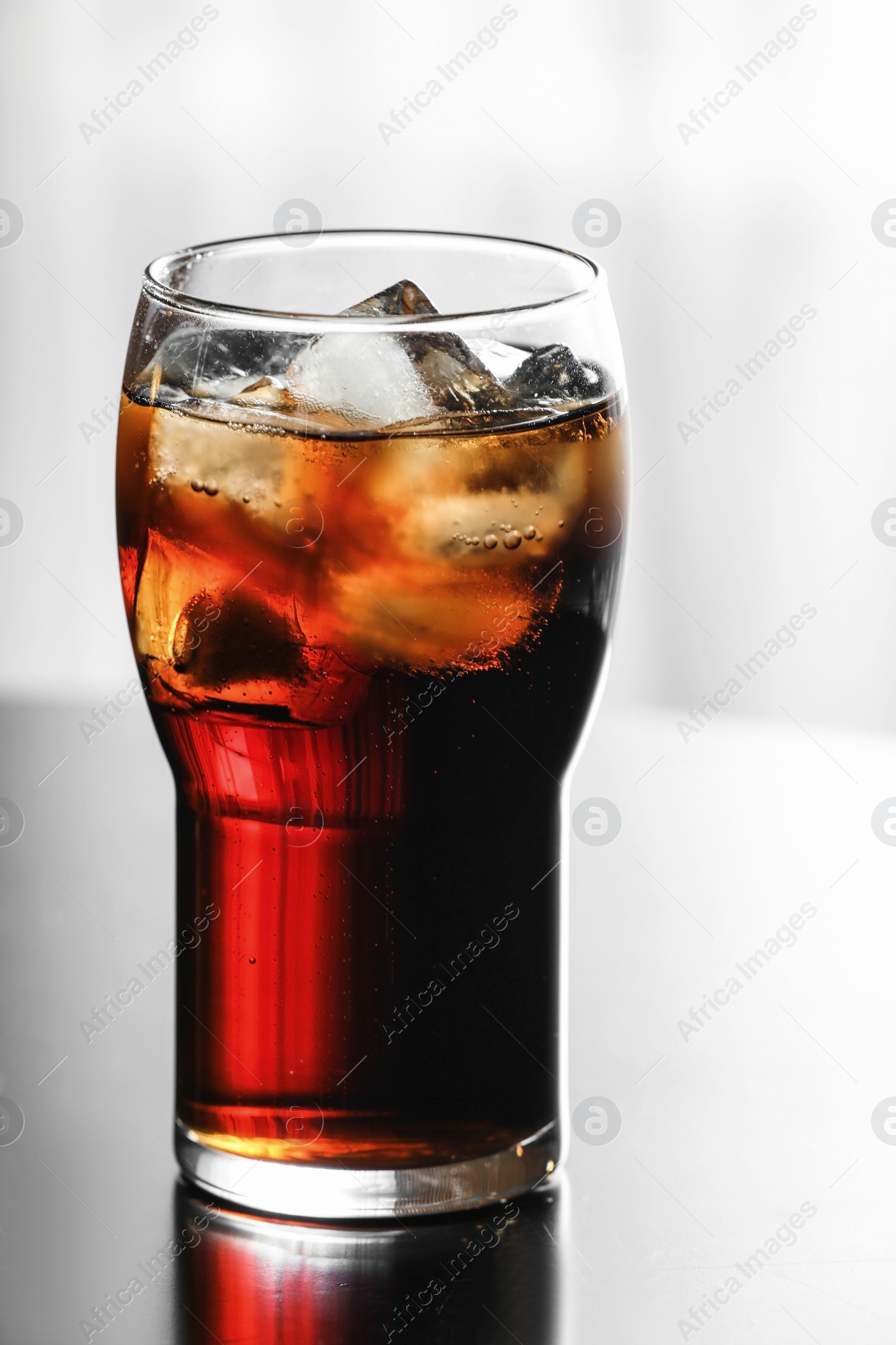 Photo of Glass of cola with ice on table against blurred background