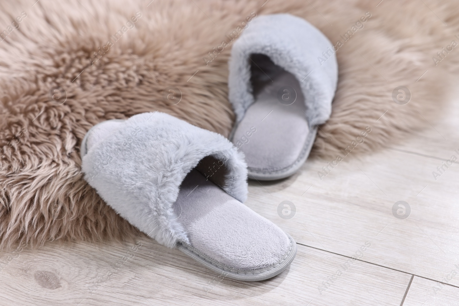 Photo of Grey soft slippers on light wooden floor at home, closeup