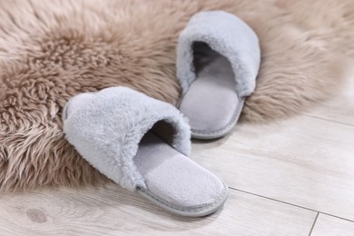 Grey soft slippers on light wooden floor at home, closeup