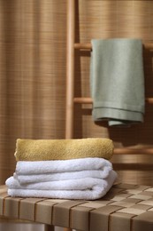 Photo of Stacked soft towels on wicker bench indoors