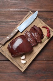 Photo of Cut raw beef liver with chili pepper, garlic and knife on wooden table, top view