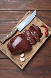 Cut raw beef liver with chili pepper, garlic and knife on wooden table, top view