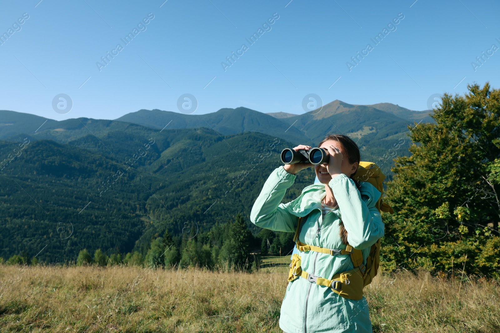 Photo of Tourist with hiking equipment looking through binoculars in mountains