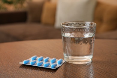 Photo of Glass of water and pills on wooden table indoors, space for text. Potency problem concept