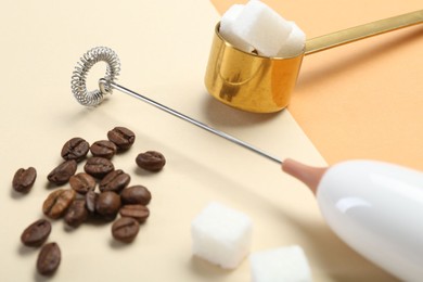 Milk frother wand, coffee beans and sugar cubes on color background, closeup