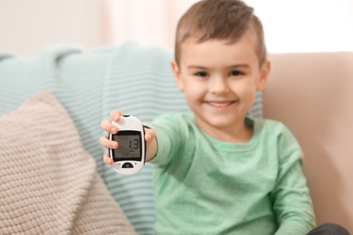 Photo of Little boy holding digital glucose meter at home, focus on hand. Diabetes control