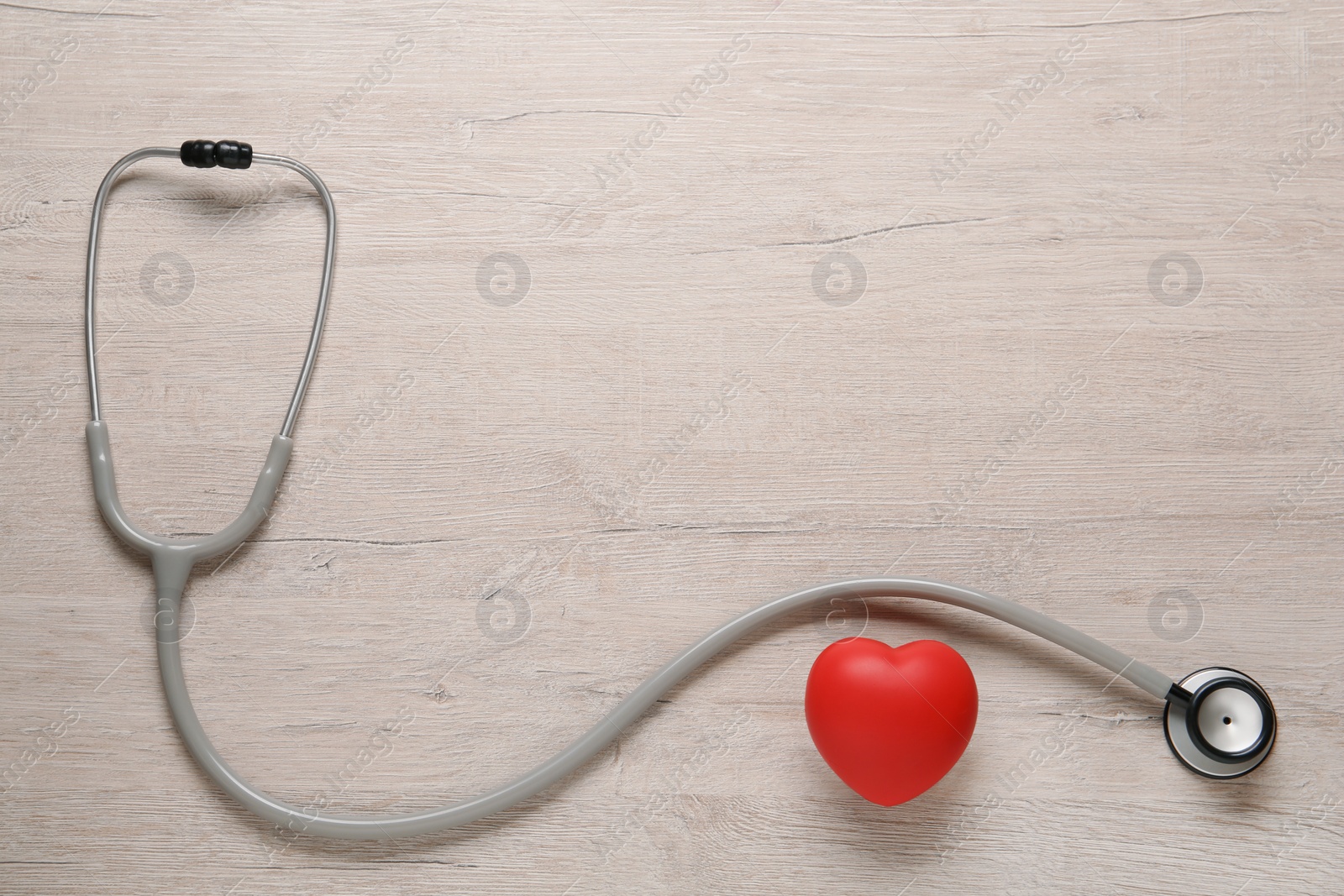 Photo of Stethoscope, red decorative heart and space for text on wooden background, flat lay. Cardiology concept