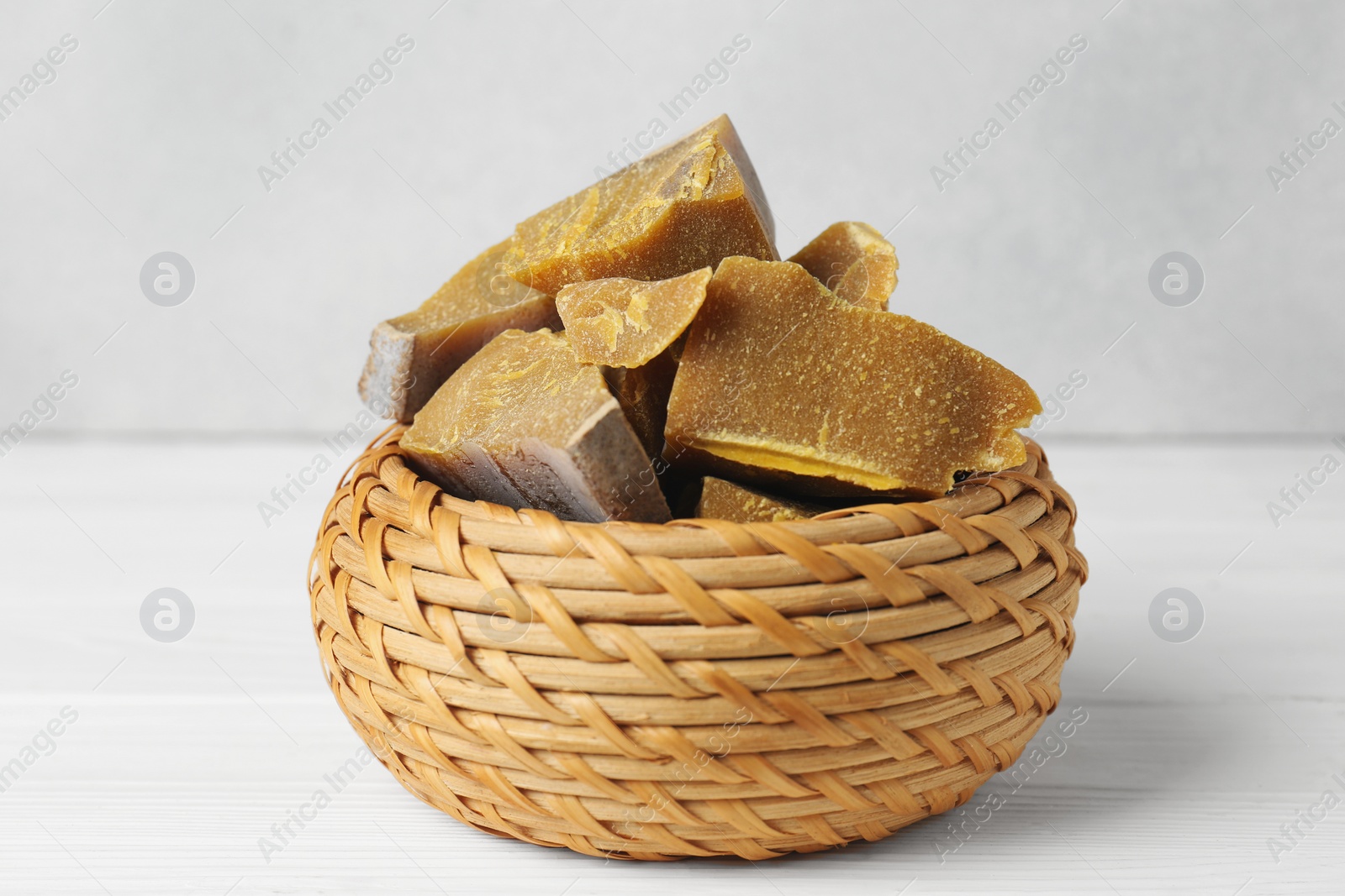 Photo of Wicker basket with natural organic beeswax blocks on white wooden table