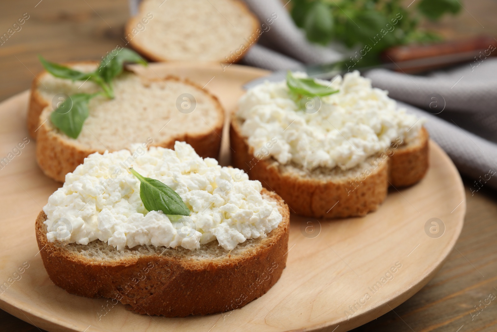 Photo of Bread with cottage cheese and basil on wooden table, closeup