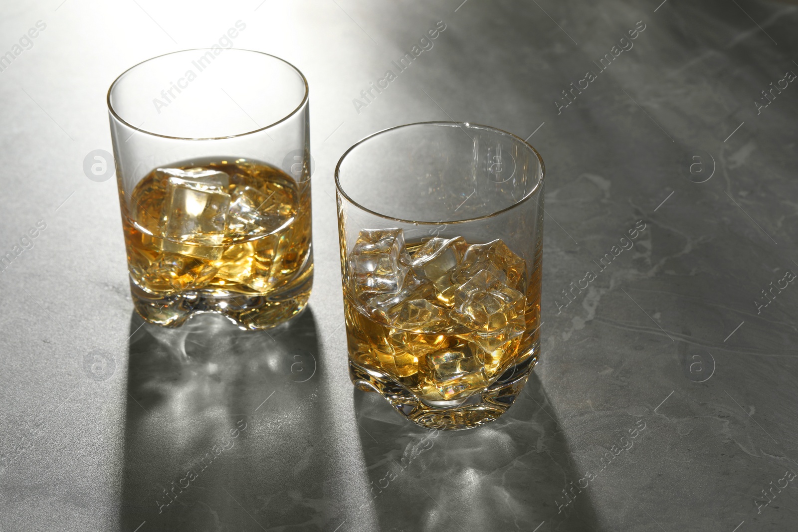 Photo of Whiskey with ice cubes in glasses on grey marble table