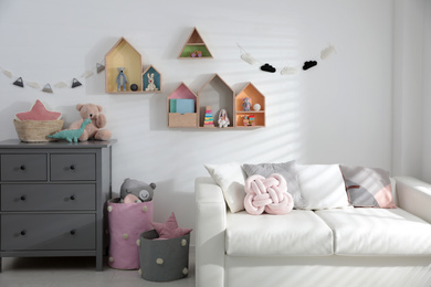 Photo of Cute children's room with house shaped shelves, sofa and chest of drawers. Interior design