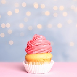 Tasty birthday cupcake with cream on table against festive lights