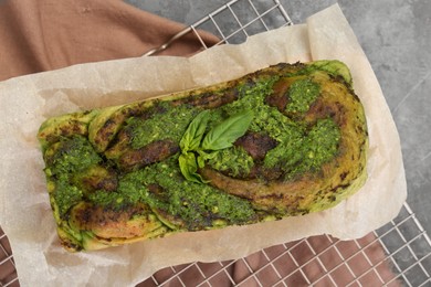 Freshly baked pesto bread with basil on grey table, top view