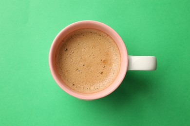 Aromatic coffee in cup on green background, top view