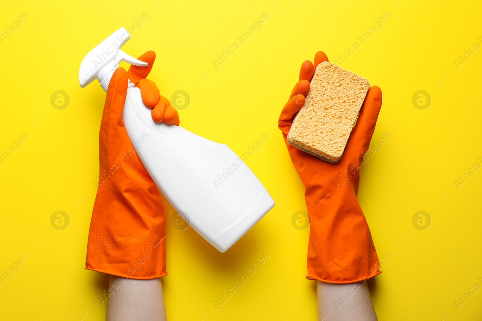 Photo of Woman in rubber gloves holding sponge and detergent on yellow background, top view