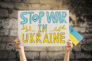 Photo of Boy holding poster Stop War In Ukraine and national flag against brick wall outdoors, closeup