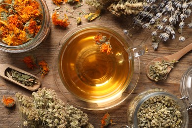 Photo of Freshly brewed tea and dried herbs on wooden table, flat lay