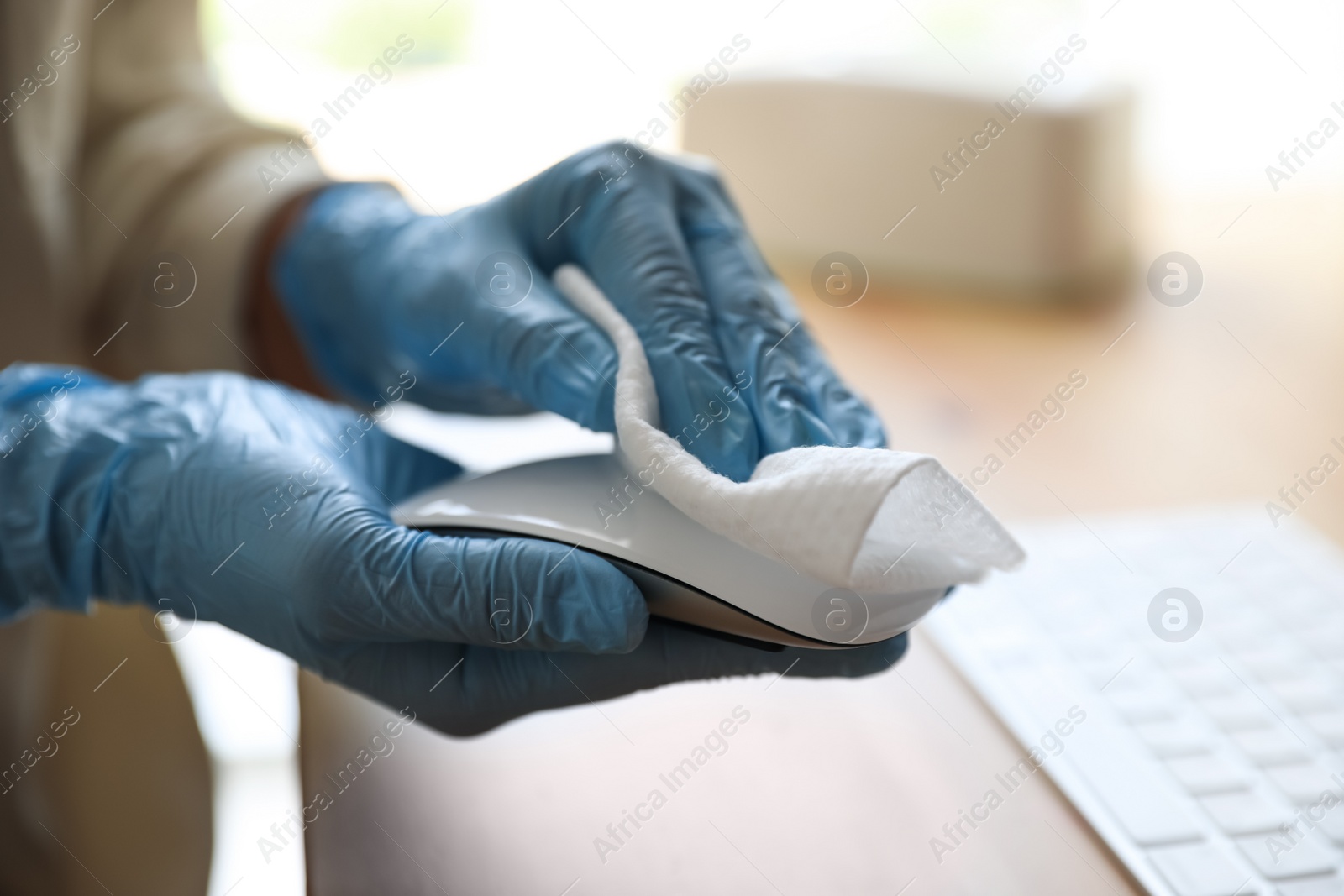 Photo of Woman in latex gloves cleaning computer mouse with wet wipe at table, closeup