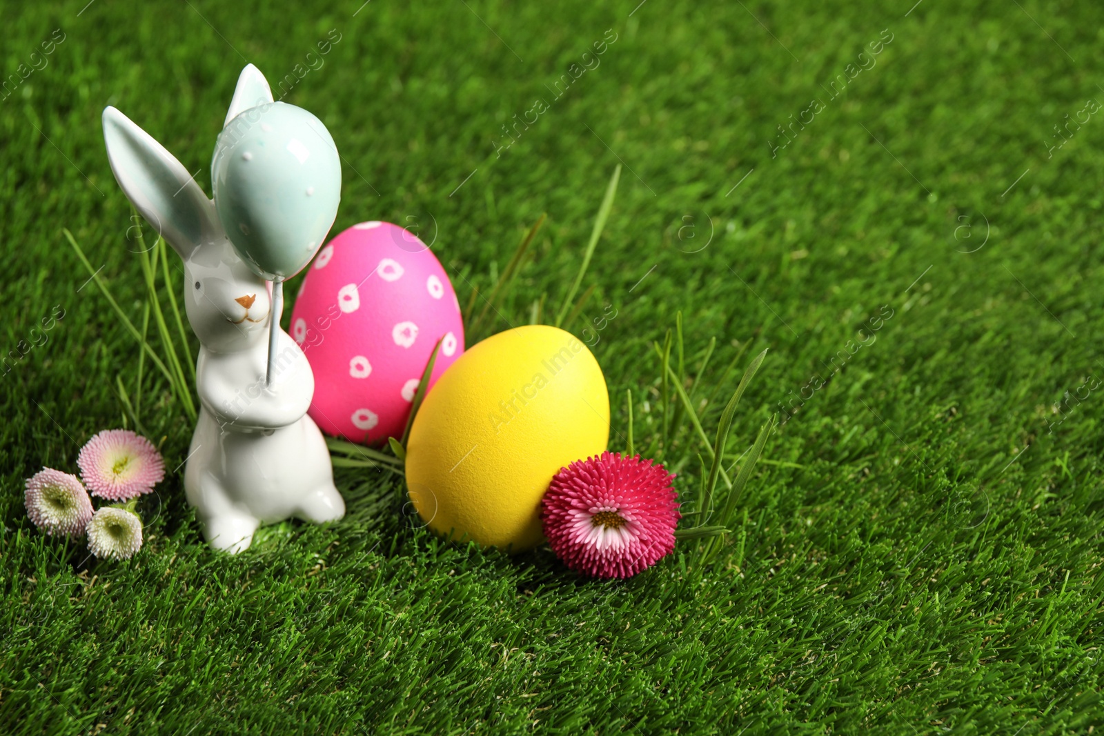 Photo of Colorful Easter eggs, rabbit and daisy flowers on green grass. Space for text