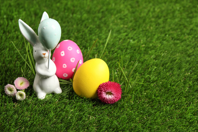 Colorful Easter eggs, rabbit and daisy flowers on green grass. Space for text