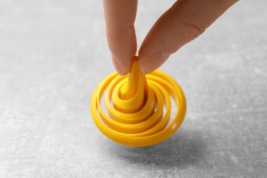 Woman playing with yellow spinning top at grey textured background, closeup