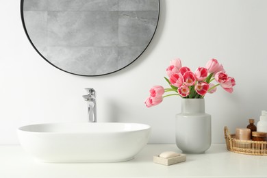 Vase with beautiful pink tulips and toiletries near sink in bathroom