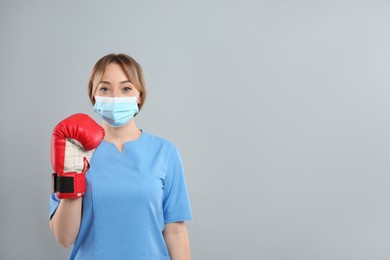 Photo of Doctor with protective mask and boxing gloves on light grey background, space for text. Strong immunity concept