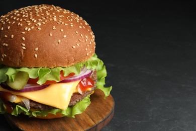 Delicious burger with beef patty and lettuce on dark table, space for text